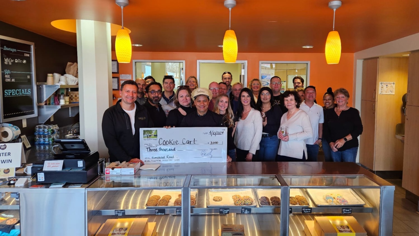 Homestead Road team members presenting a three thousand dollar donation check to Cookie Cart inside the Cookie Cart bakery in Minneapolis