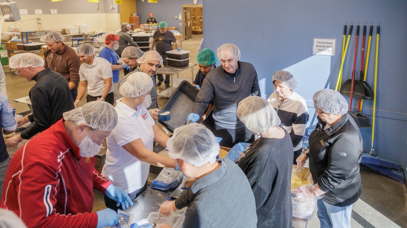 Volunteers in hairnets and gloves packing meals of rice and dry ingredients at a Feed My Starving Children packing station